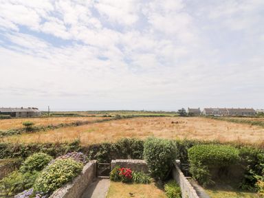 A garden with shrubs and flowers overlooking a field with houses in the distance at Boslow in St Just