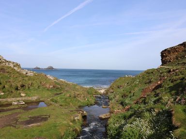 A coastal landscape with grassy hills a small stream flowing into the sea and rocky outcrops at Boslow in St Just