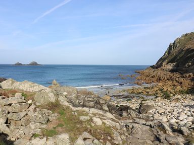 A rocky coastline with a pebble beach and two small islands in the sea at Boslow in St Just