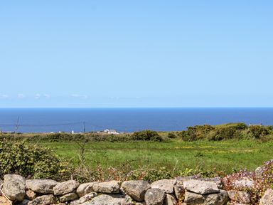 A stone wall with green fields and bushes beyond and the sea in the background at Boslow in St Just