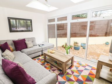 A living room with a grey sectional sofa and colorful cushions a wooden coffee table with flowers next to large windows at Higher Kernick Stable in Helland near Blisland
