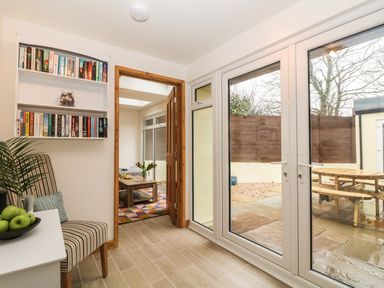 A room with a striped chair a small table with green apples shelves with books a door leading to another room and glass doors opening to a patio at Higher Kernick Stable Helland near Blisland