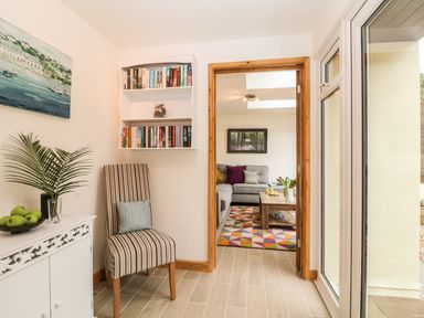 A hallway with a striped chair a white cabinet with a plant and apples a bookshelf and a view into a living room at Higher Kernick Stable Helland near Blisland