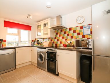 A kitchen with white cabinets colorful tile backsplash and various appliances at Higher Kernick Stable Helland near Blisland