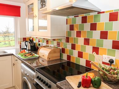 A kitchen with a stove a wooden bread box colorful tiled backsplash and vegetables on a cutting board at Higher Kernick Stable Helland near Blisland