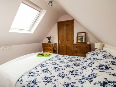 A bedroom with a slanted ceiling a skylight bed with floral bedding two wooden dressers a door and a lamp at Higher Kernick Stable Helland near Blisland