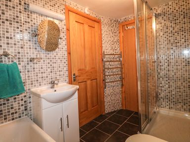 A bathroom with a sink cabinet a round mirror wooden doors a towel rail a shower enclosure and tiled walls at Higher Kernick Stable in Helland near Blisland