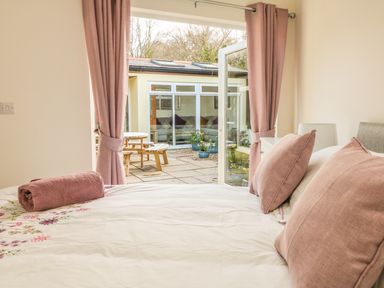 A bedroom with an open door to a patio with wooden table and chairs at Higher Kernick Stable Helland near Blisland