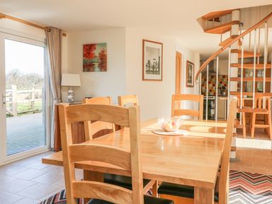 A dining room with a wooden table and chairs near a glass door and a spiral staircase at Higher Kernick Stable in Helland near Blisland