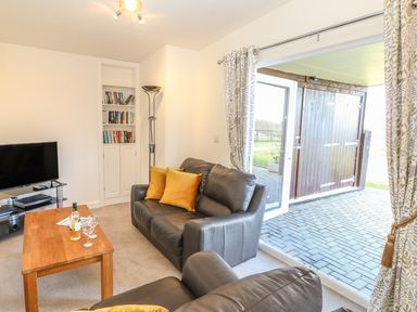 A living room with a leather sofa and armchair yellow cushions wooden coffee table television bookshelf and glass door leading outside at Higher Kernick Stable Helland near Blisland