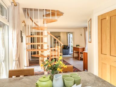 A dining area with a spiral staircase and a living room in the background at Higher Kernick Stable in Helland near Blisland