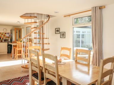 A dining area with a wooden table and chairs next to a spiral staircase and kitchen at Higher Kernick Stable Helland near Blisland