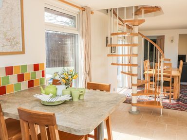 A kitchen area with a table set with green mugs and a teapot next to a spiral staircase and a dining table with chairs at Higher Kernick Stable in Helland near Blisland