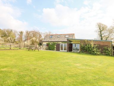 A large grassy yard with a wooden picnic table and a house with skylights and sliding glass doors at Higher Kernick Stable in Helland near Blisland