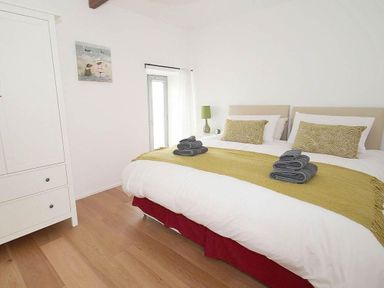 A bedroom with a double bed with white bedding green throw and pillows next to a white wardrobe at The Old Dairy in Padstow