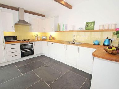 A kitchen with white cabinets wooden countertops yellow tile backsplash and black stone floor at The Old Dairy in Padstow