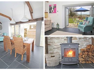 A dining area with wooden table and wicker chairs a sitting area with armchair and open doors to garden and wood burning stove with fire and firewood at The Old Dairy in Padstow