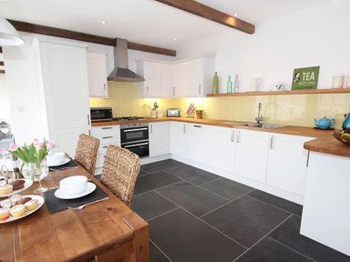 A kitchen with white cabinets wooden countertops and a dining table with chairs at The Old Dairy in Padstow
