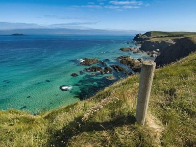 A coastal cliff with grass and a wooden post overlooking rocky shoreline and blue sea at The Old Dairy in Padstow