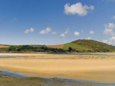 A sandy beach with a hill and fields under a blue sky at The Old Dairy in Padstow