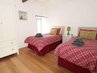 A bedroom with two single beds with red plaid bedding and a white wardrobe at The Old Dairy in Padstow