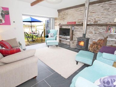 A living room with armchairs a sofa a wood-burning stove and an open door to a patio at The Old Dairy in Padstow