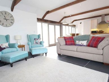 A living room with blue armchairs a beige sofa and a large clock on the wall at The Old Dairy in Padstow