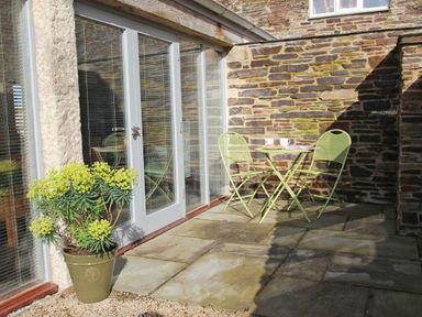 A small patio with a green potted plant and green metal table and chairs outside a stone wall building at The Old Dairy in Padstow