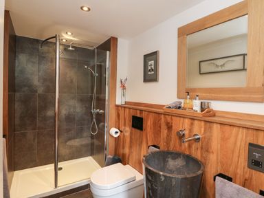 A bathroom with a glass shower enclosure wooden paneling a toilet and a stone sink at Hideaway Watergate Bay