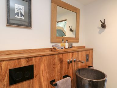 A bathroom with a wooden panel wall a black stone sink a wooden framed mirror hand soap and lotion on a tray and a framed Vogue cover at Hideaway Watergate Bay