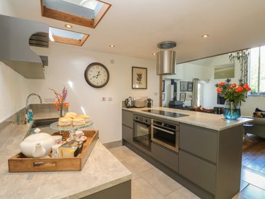 A kitchen with a teapot on a wooden tray and flowers on the countertop at Hideaway in Watergate Bay