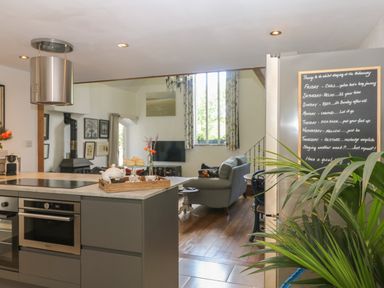 A kitchen with a stove and oven island next to a living area with a sofa and television at Hideaway in Watergate Bay