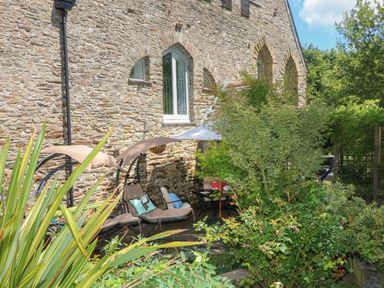 An outdoor patio area with hanging lounge chairs and plants next to a stone building at Hideaway in Watergate Bay
