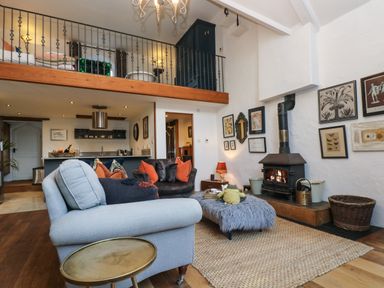 A living room with a wood stove a gray armchair a furcovered ottoman and framed pictures on the wall at Hideaway in Watergate Bay