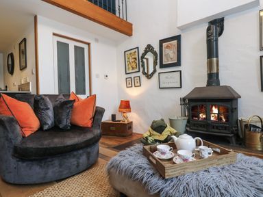 A living room with a fireplace a round dark sofa with orange and grey cushions and a tea set on a tray on a furry ottoman at Hideaway in Watergate Bay