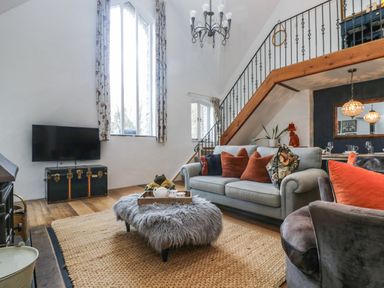 A living room with a grey sofa and orange pillows a TV on a chest and a fur-covered ottoman at Hideaway in Watergate Bay