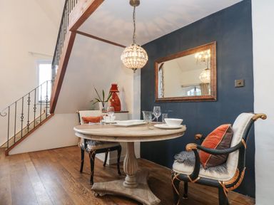A dining area with a round wooden table and two chairs under a hanging light and a large mirror on a dark wall at Hideaway in Watergate Bay