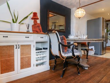 A dining area with chairs and a round table next to a cabinet with a plant and lamp at Hideaway in Watergate Bay