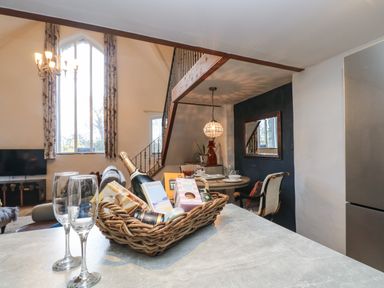 A dining area with a round table and chairs behind a kitchen counter with a basket of food items and two empty glasses at Hideaway in Watergate Bay