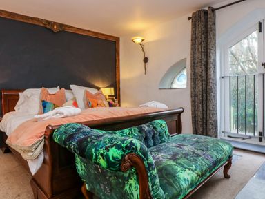 A bedroom with a wooden bed and colorful pillows and a green patterned sofa at Hideaway in Watergate Bay