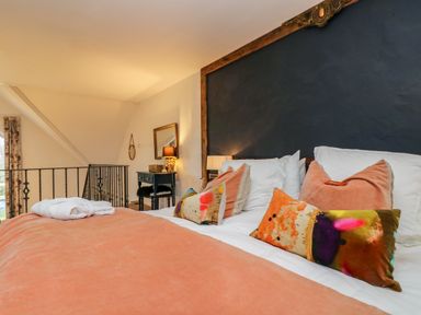 A bedroom with a double bed with colorful pillows and a peach blanket next to a black wall and a small desk with a lamp at Hideaway in Watergate Bay