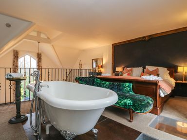 A bedroom with a clawfoot bathtub near a green velvet bench and a large bed at Hideaway in Watergate Bay