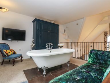 A room with a freestanding white bathtub a blue armchair a dark green sofa and a wall-mounted television at Hideaway in Watergate Bay