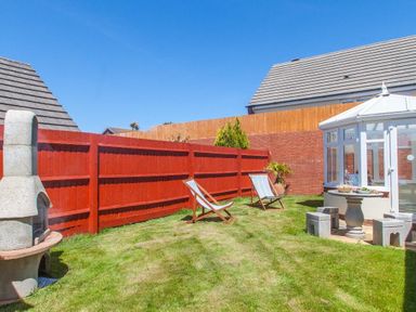 A backyard with two deck chairs a patio table with stools a barbecue grill and a conservatory at Fairways in Woolacombe