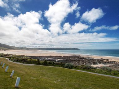 A sandy beach with rocky outcrops and green grassy area under a partly cloudy sky at Fairways in Woolacombe