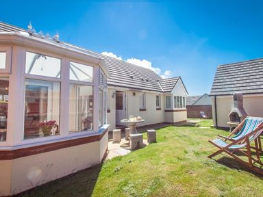 A backyard with a patio table and stools a conservatory and deck chairs at Fairways in Woolacombe