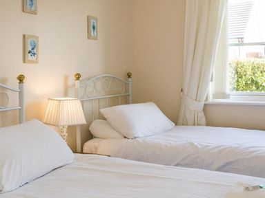 A bedroom with two single beds a lamp on a bedside table and a window with curtains at Fairways in Woolacombe
