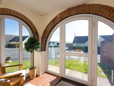 A sunroom with arched windows wooden chairs a potted plant and a view of a street outside at Fairways in Woolacombe