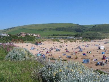 A sandy beach with people and tents near green hills at Fairways in Woolacombe