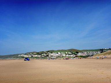 A sandy beach with people and a blue tent near a coastal town with houses on grassy hills at Fairways in Woolacombe